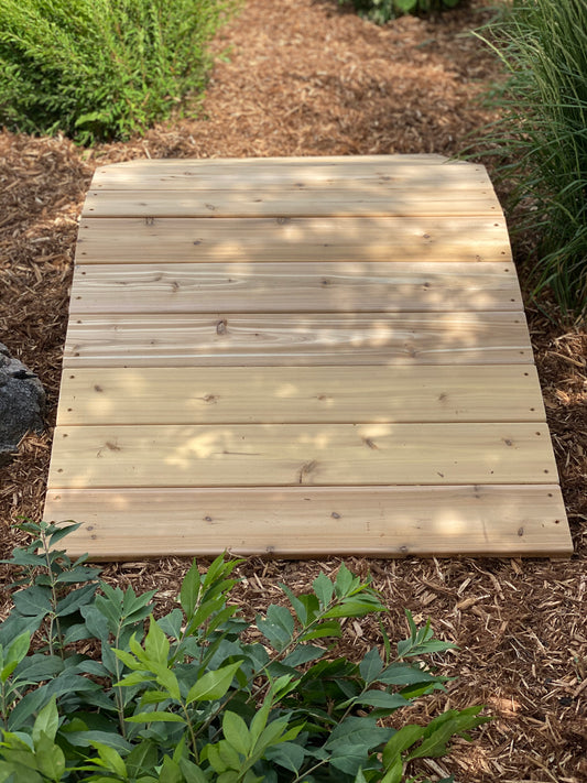 A wooden outdoor ramp designed for children's play, situated on a natural outdoor surface.