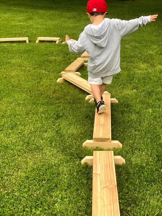 Young child balancing carefully on a low wooden beam outdoors, developing coordination and confidence through risky play.