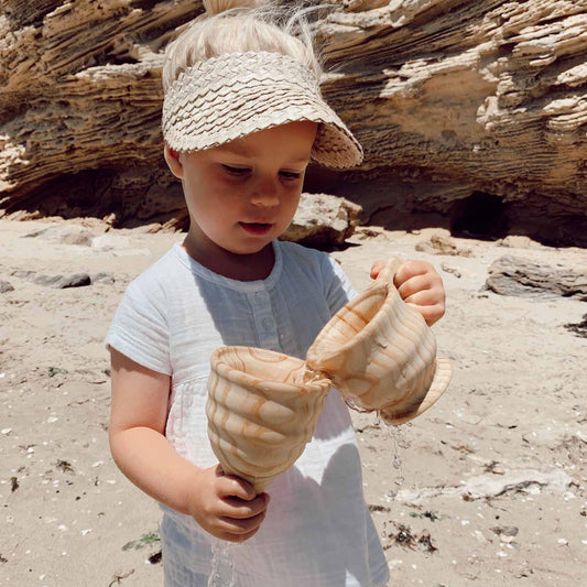 Child holding a wooden funnel and cup set for outdoor water play