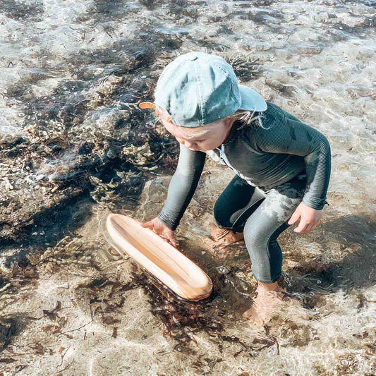 Child playing with a wooden toy boat during outdoor water play