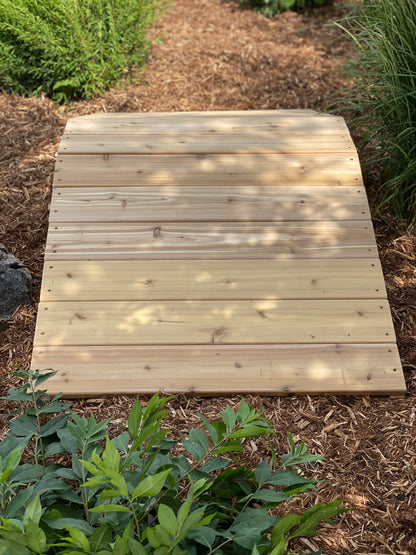 A wooden outdoor ramp designed for children's play, situated on a natural outdoor surface.